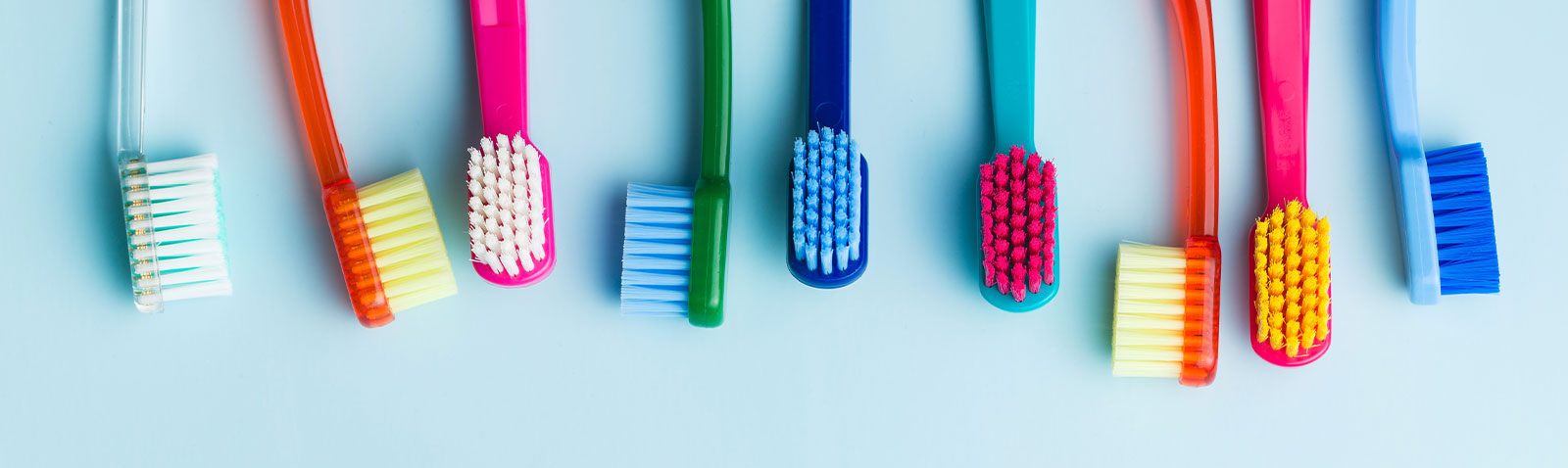 The image shows a collection of colorful toothbrushes arranged on a surface with a plain background.