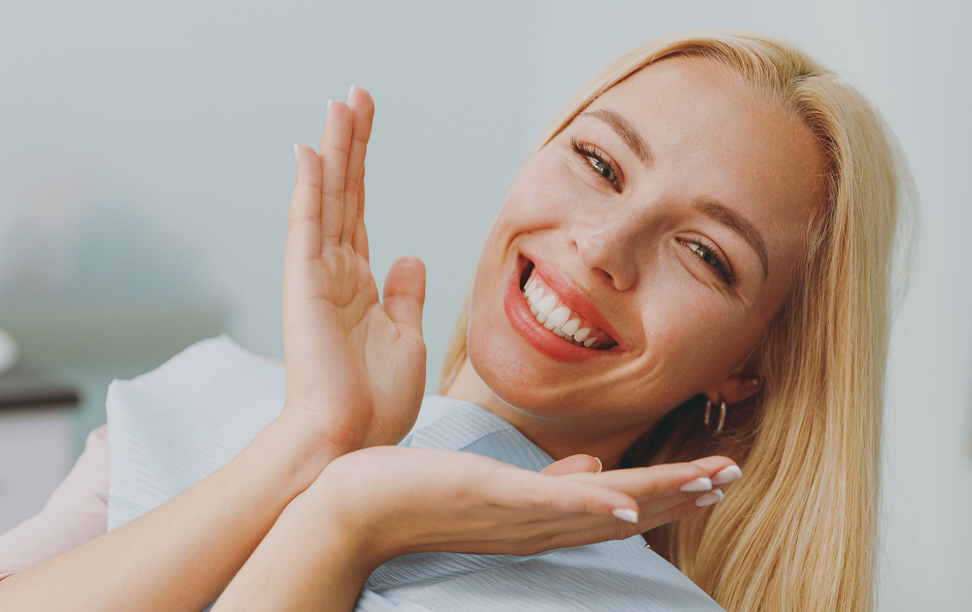 A smiling woman with blonde hair, wearing a white top, sitting in front of a blue background.