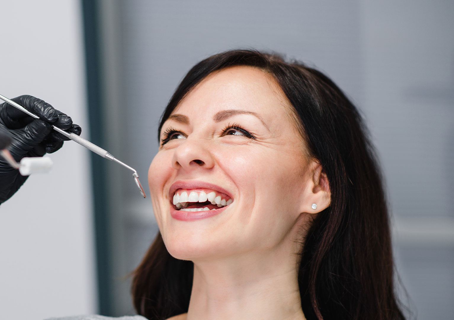 A woman receiving dental care, with a smiley expression, while a dental professional applies a treatment using a syringe.