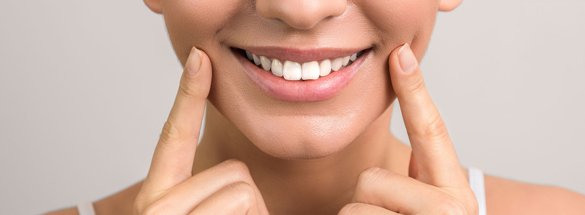 A smiling woman with her hands on her cheeks, showcasing a product or service related to dental care or beauty.
