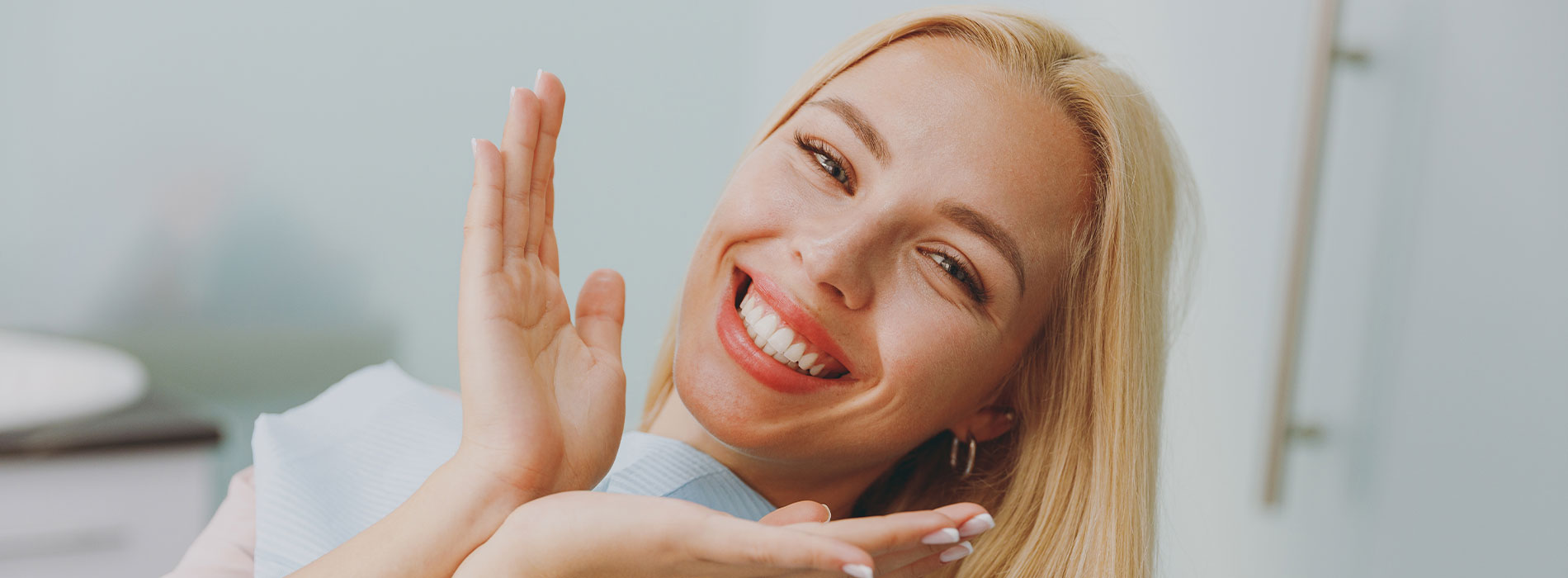 A woman with blonde hair smiling at the camera while holding her hand up to her face.