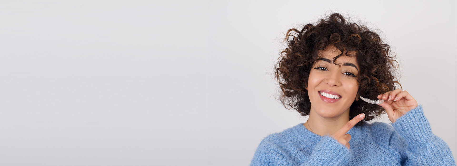 A person with curly hair, smiling, in front of a plain background.