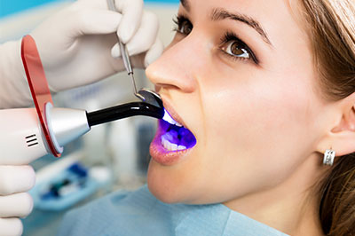 The image shows a person sitting in a dental chair with a dentist's hand holding a device over their mouth, which appears to be part of a dental examination or treatment process.