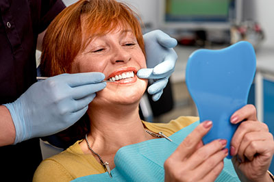 A woman receiving dental care, with a dental hygienist applying a blue mouthguard while she smiles, with medical equipment and a professional setting visible.