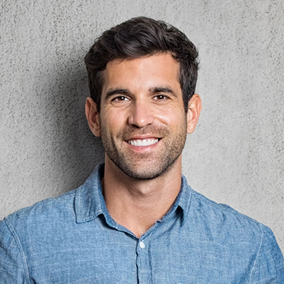 The image depicts a smiling man with short hair and a beard, wearing a denim shirt, posing against a gray background.