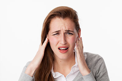 The image shows a woman with her hand on her ear, appearing to be in pain or discomfort, with an expression of distress or concern.