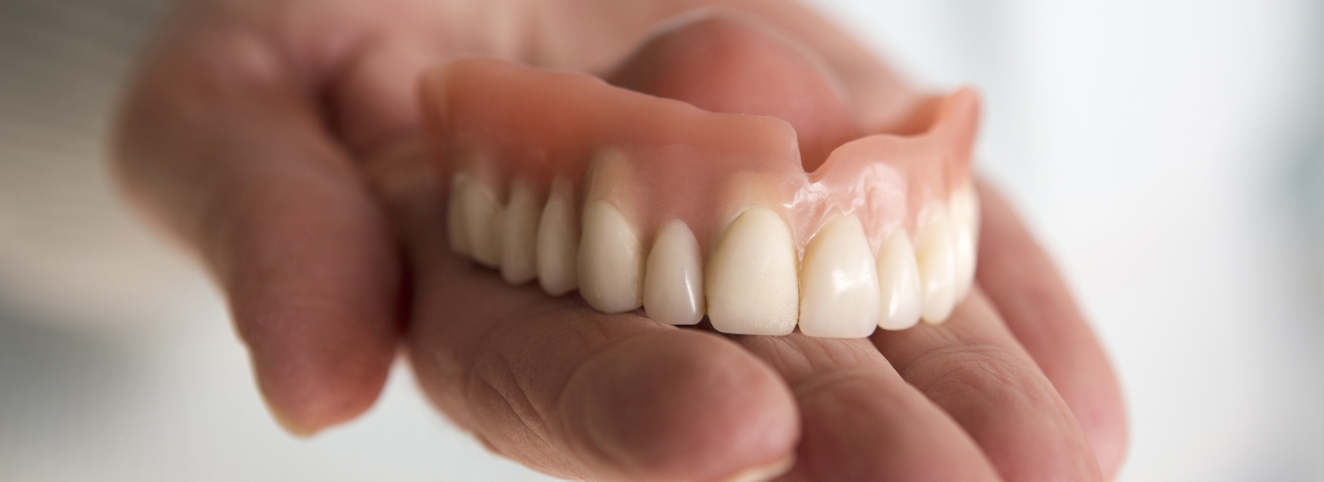 A person holds up a set of dentures with an open mouth displaying the teeth.