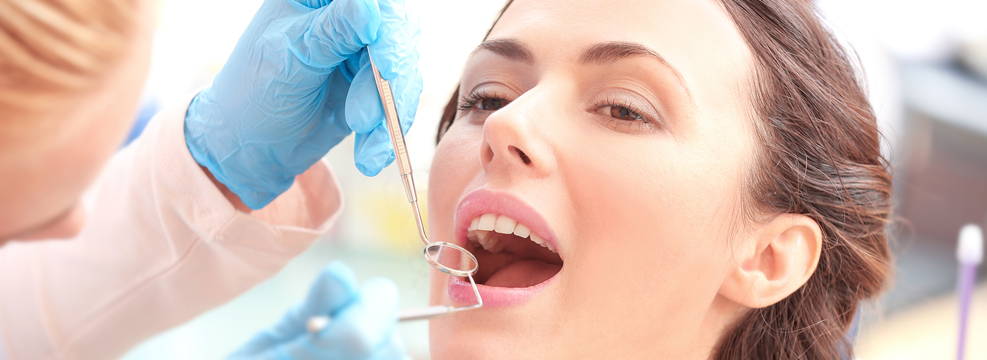 The image shows a professional dental setting where a woman is receiving dental care, with a dental hygienist performing a cleaning procedure on her teeth while she sits comfortably in the chair.