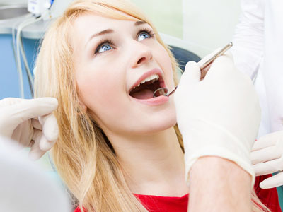 A young woman with open mouth undergoing dental treatment while sitting in a dentist's chair.