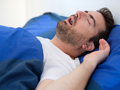 A man sleeping on a bed with a blue comforter.